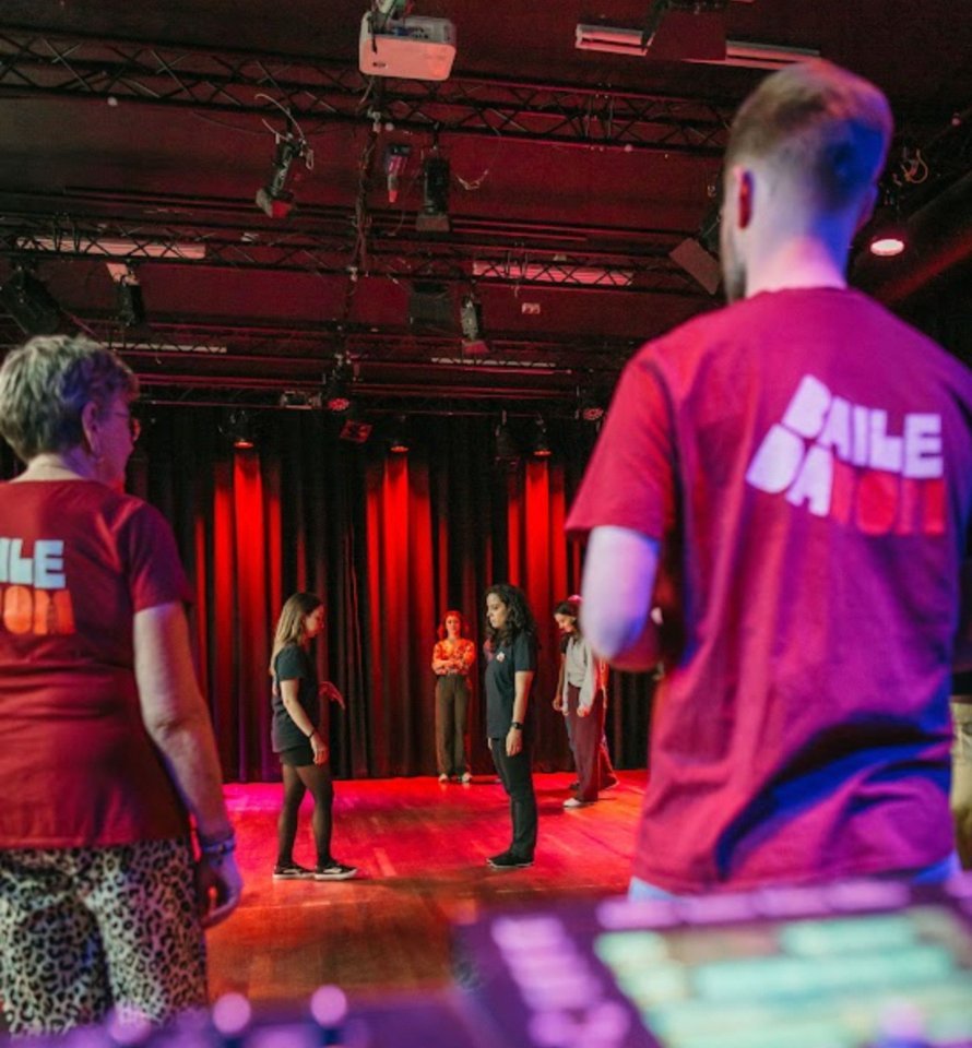 A teacher in the burgundy Baile da Dom t-shirt, showing the large logo on the back, during a class